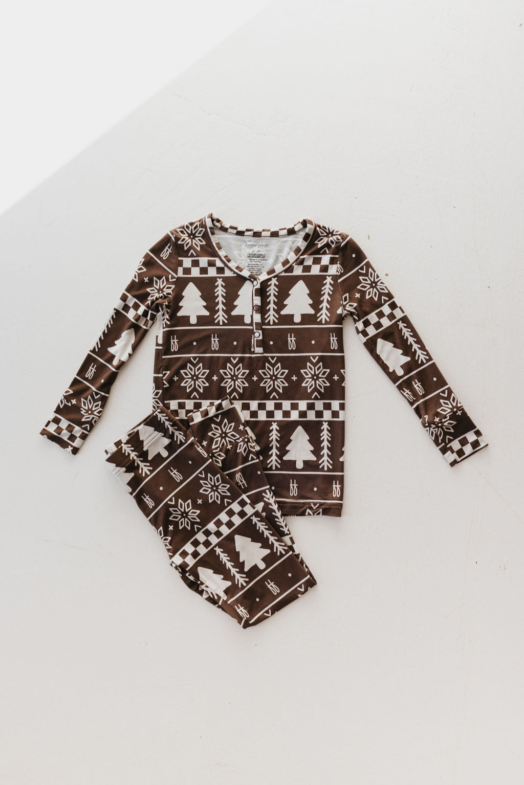 Brown toddler pajamas from Forever French Baby, known as the Bamboo Two Piece Pajamas in the Forever Fair Isle design, crafted from breathable bamboo fabric and featuring a white winter pattern with snowflakes and pine trees, laid flat on a white background.