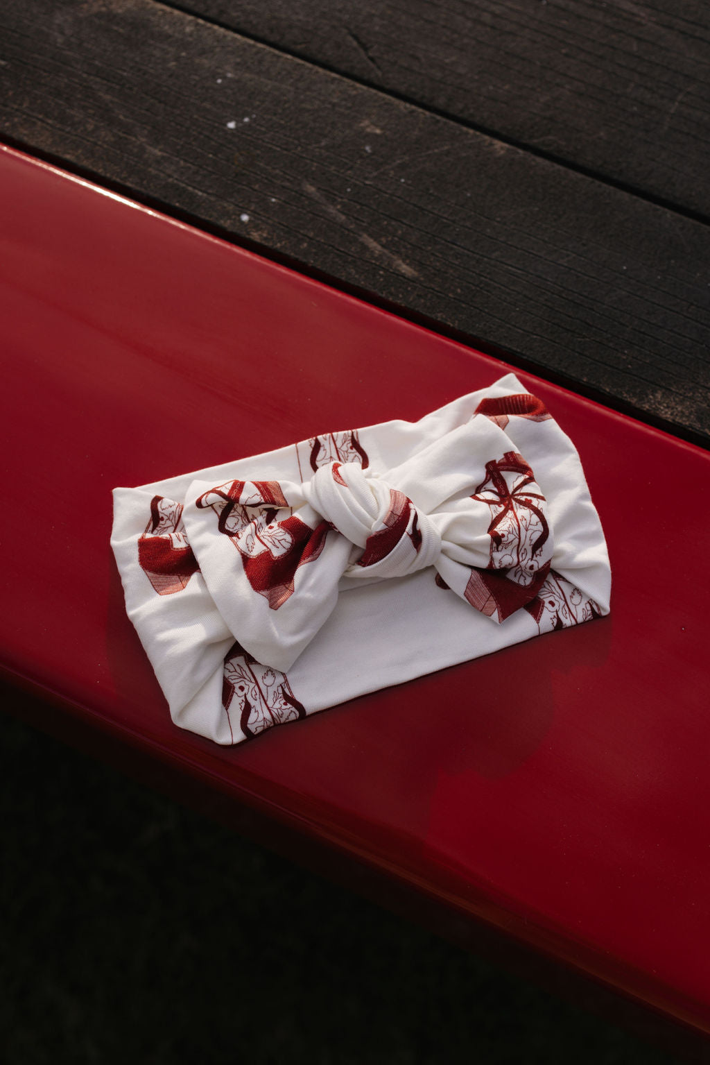 A Bamboo Head Wrap | Cowgirl Christmas by lolo webb, featuring a stylish pattern and central knot, is displayed on a red surface with a dark wooden background.