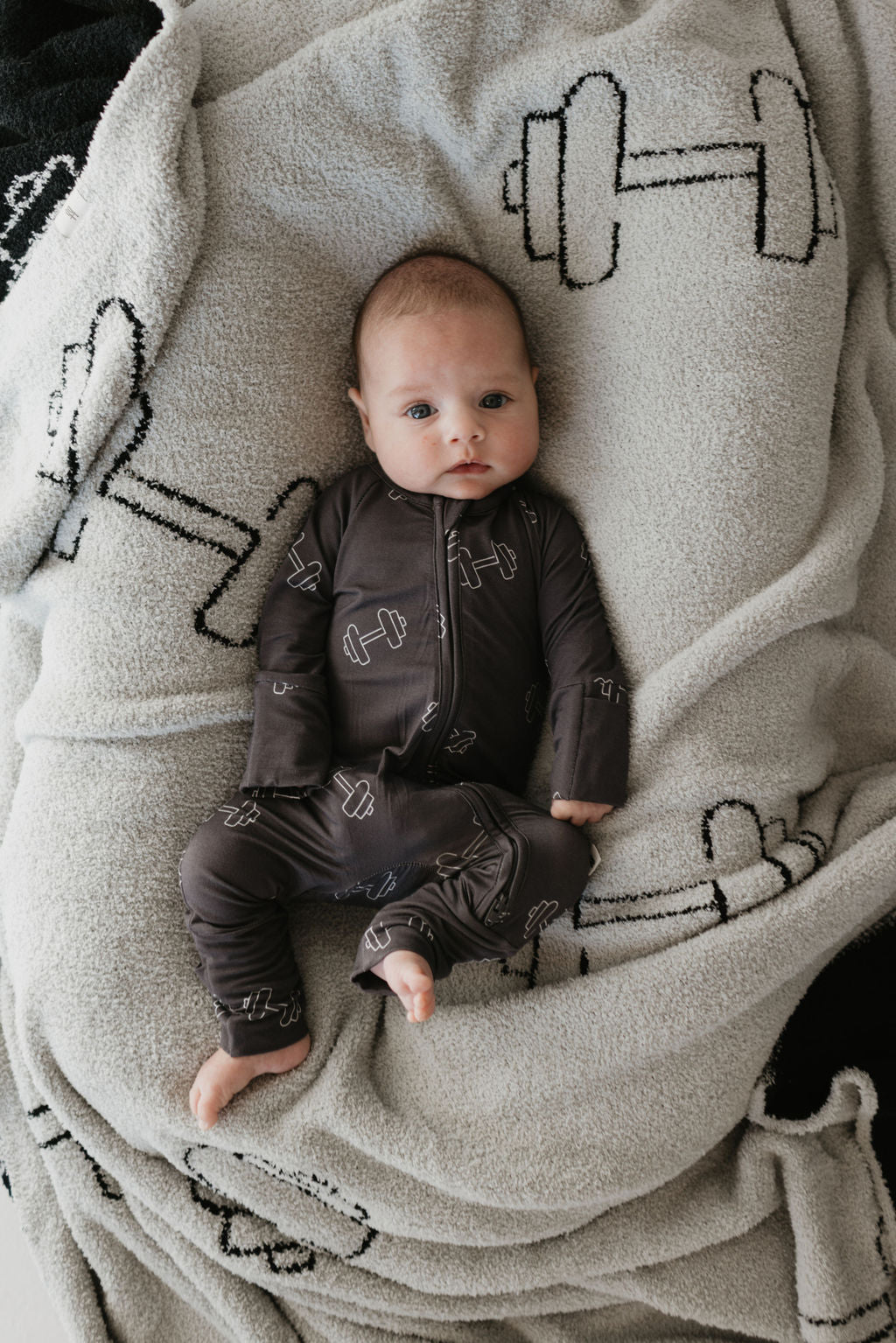 A baby in the Bamboo Zip Pajamas by forever french baby lies contentedly on a blanket, wrapped in the gentle embrace of hypo-allergenic clothing.