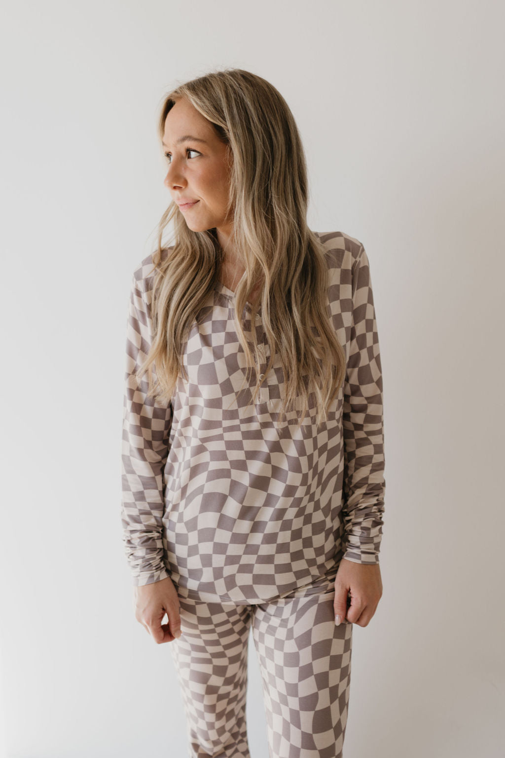 A person with long hair stands against a white background, dressed in breathable clothing: the Women's Bamboo Pajamas in Smokey Wave by forever french baby, looking to the side.