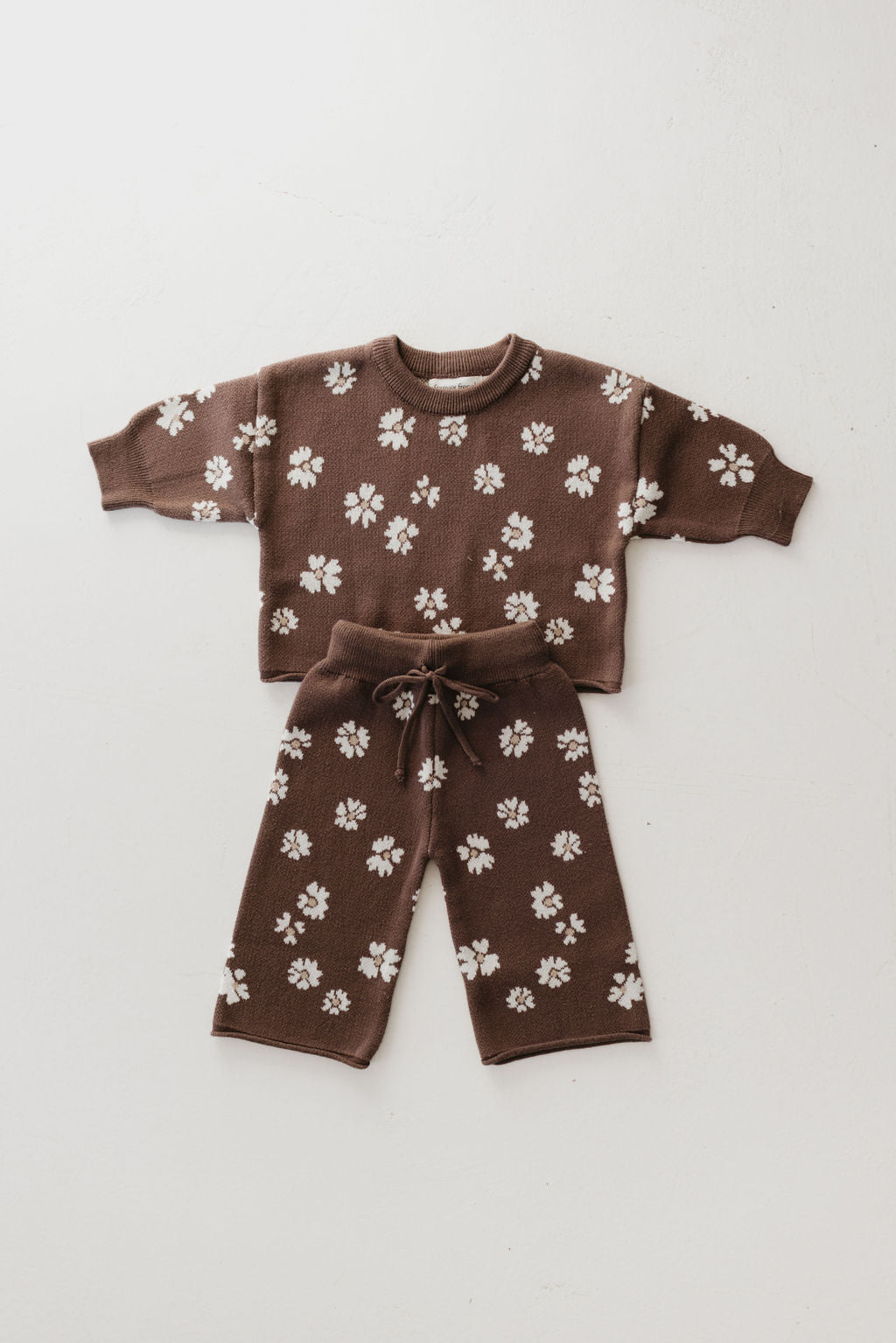 Discover the adorable "Midnight Meadow" Knit Pant Set by forever french baby, a delightful two-piece outfit featuring a sweater and pants in brown with a charming white floral pattern. This stylish set, made from 100% cotton, is perfect for enhancing any child's fall wardrobe. Laid neatly against a neutral backdrop, it's designed to offer both comfort and style throughout the season.