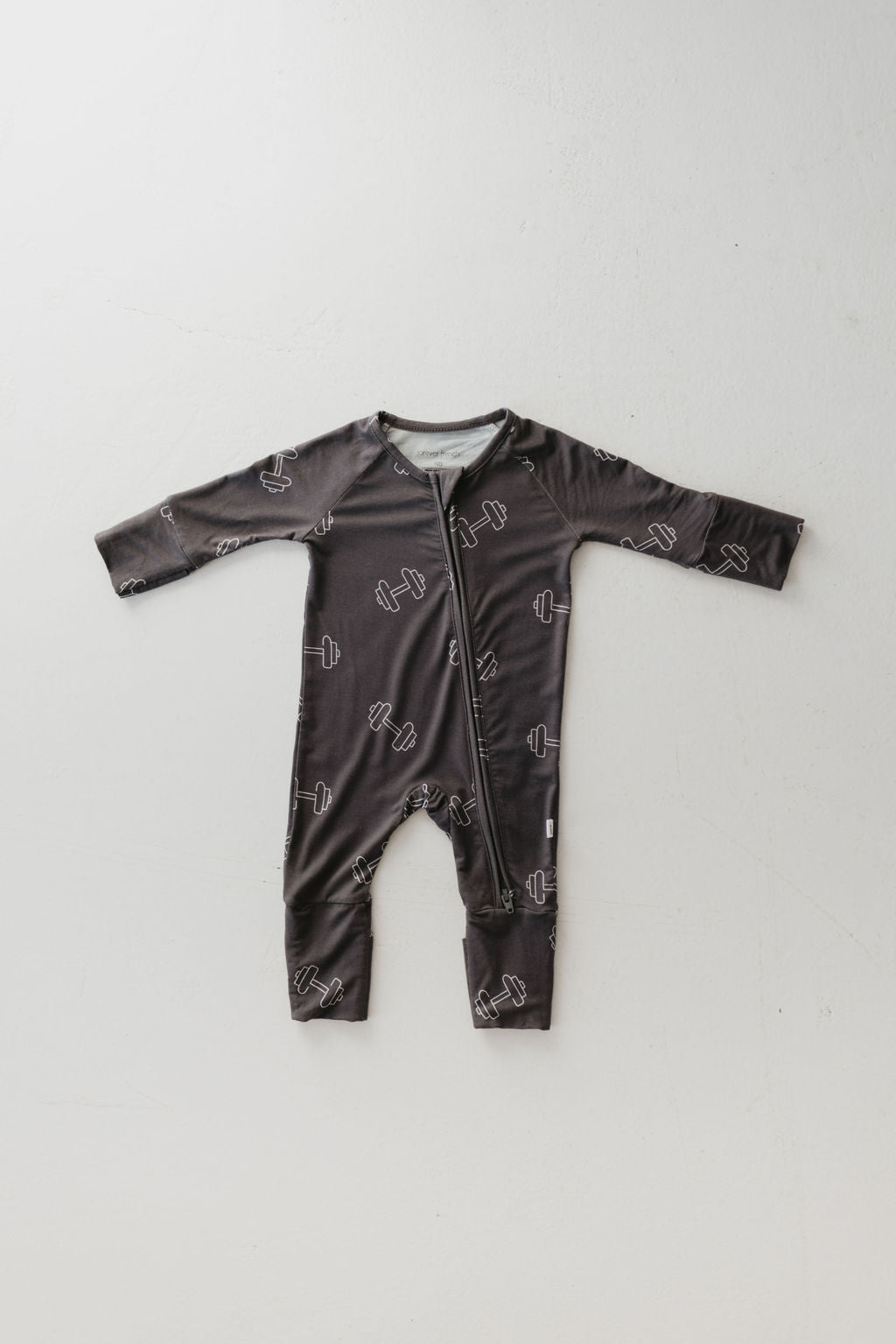 The "Charcoal Arm Day" Bamboo Zip Pajamas by forever french baby is a dark gray, hypo-allergenic long-sleeve onesie with white dumbbell patterns and front zipper, shown on a light background.