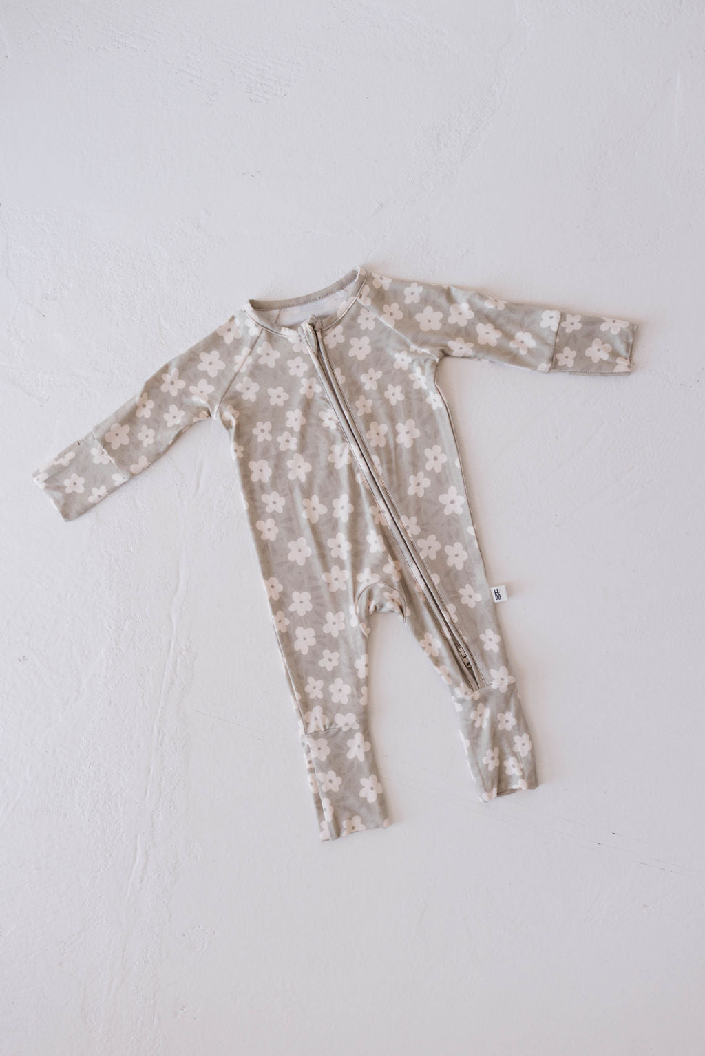 A French Gray Floral full-length baby romper from forever french baby lies flat on a white surface. This cozy Bamboo Zip Pajamas piece features long sleeves, a front zipper, and a pattern of white floral designs. Made from premium bamboo material, the cuffs on the sleeves and legs are folded for added comfort.