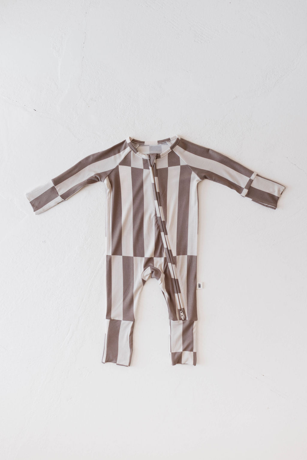 A Bamboo Zip Pajama from the Forever French Baby collection is laid flat on a white background. This long-sleeved, footless romper, made from soft premium bamboo, features a zip-up front and a pattern of wide horizontal and vertical stripes in shades of grey and beige. The design is named "Tile Stack.