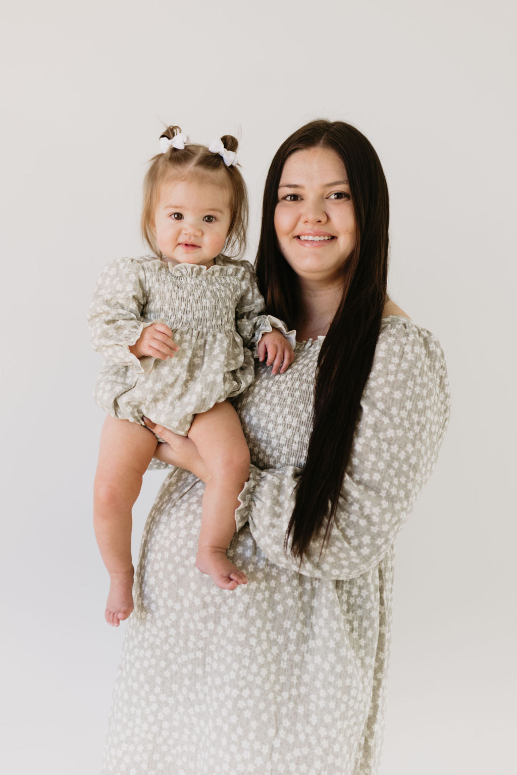 A woman with long dark hair holds a baby showcasing matching rompers in the French Gray Floral design by forever french baby. Both are smiling against a plain white background, their outfits perfectly suited for the gentle cycle.