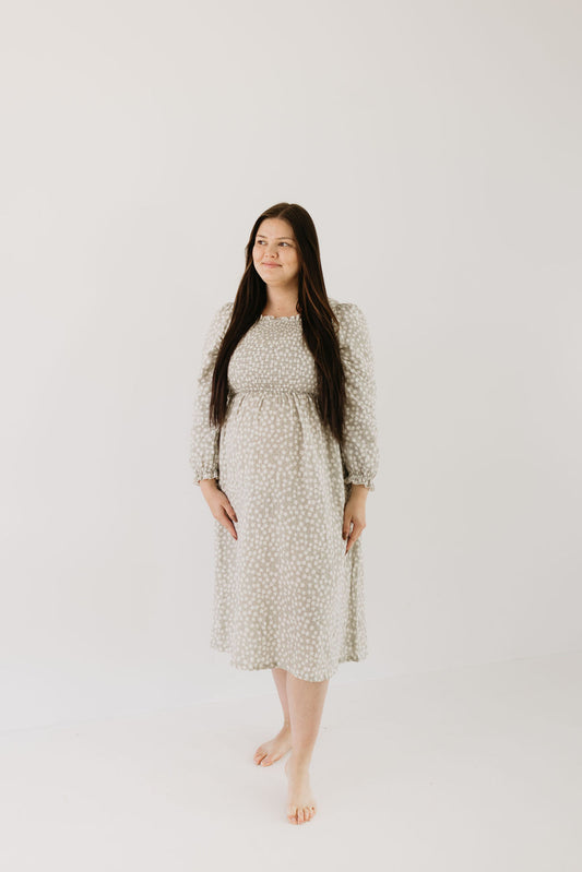 A woman with long dark hair stands barefoot in a forever french baby Adult Dress | French Gray Floral, adorned with white polka dots. She gazes off to the side against a plain white or light gray background.