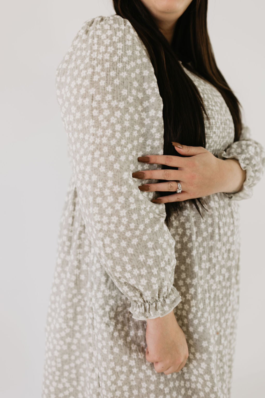 A person is wearing the forever french baby Adult Dress in French Gray Floral, with hair down and gently holding one arm. The image highlights the upper body, showcasing the dress's texture and design.