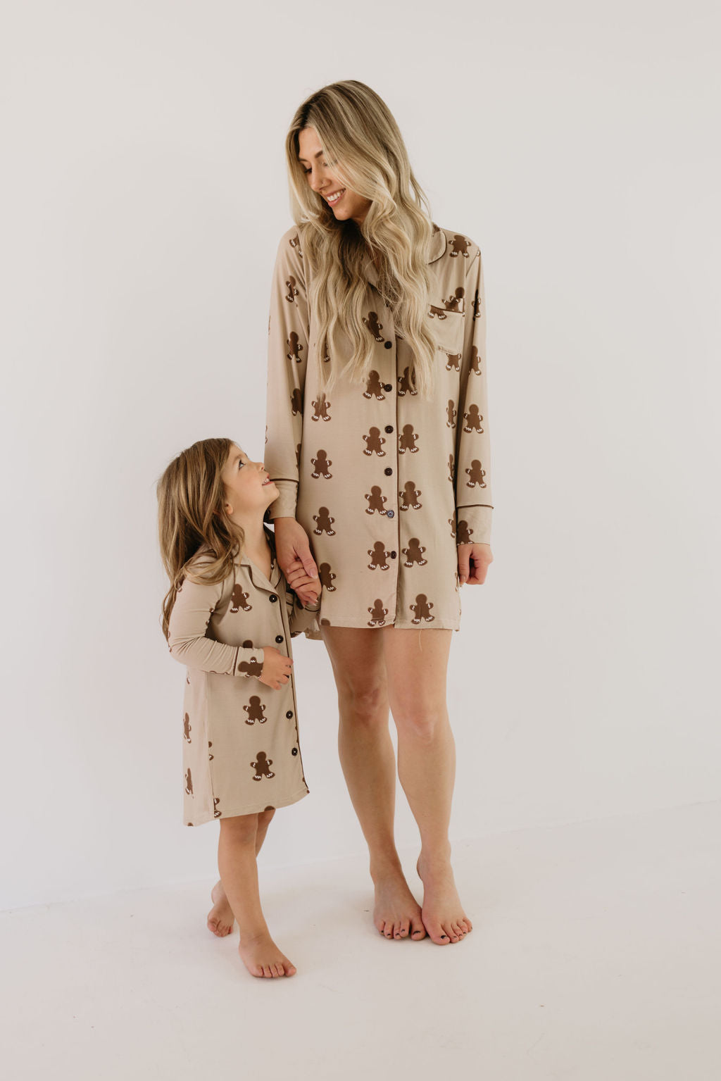 A woman and a young girl stand barefoot in matching teddy bear-patterned pajamas made from breathable bamboo fabric, embodying the comfort and joy of the Toddler Bamboo Sleeping Dress in Gingerbread by forever french baby. They hold hands, smiling at each other against a plain white background.