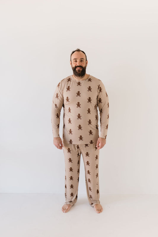 A bearded man smiles, standing barefoot in the Men's Bamboo Pajamas | Gingerbread by forever french baby. The hypo-allergenic clothing, made from breathable fabric, stands out against the plain white background.