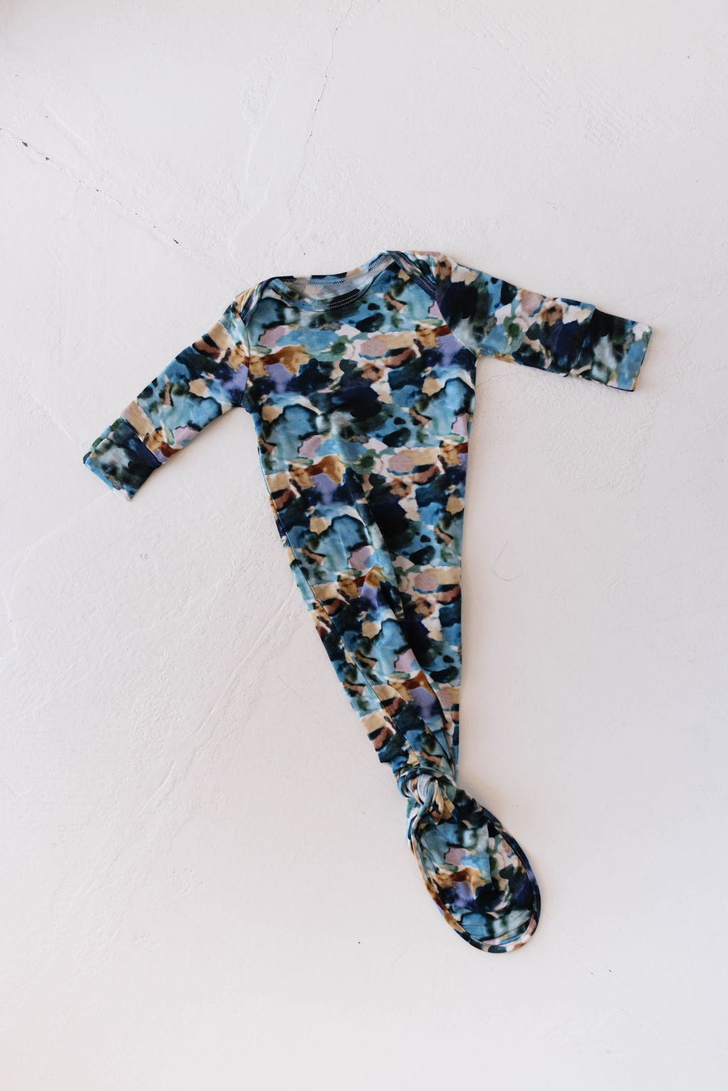 The Bamboo Knotted Gown | Charli Print by forever french baby is laid flat on a white surface. This long-sleeve gown features a colorful abstract pattern in shades of blue, green, brown, and white, reminiscent of Autistic daughter art.