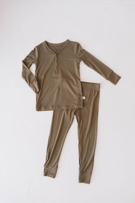 A set of long-sleeve olive green Forever French Baby Bamboo Two Piece Pajamas is laid flat against a white background. The pajama set, made from hypo-allergenic bamboo clothing, includes a henley-style top with buttons on the neckline and matching pants with an elastic waistband and cuffs.