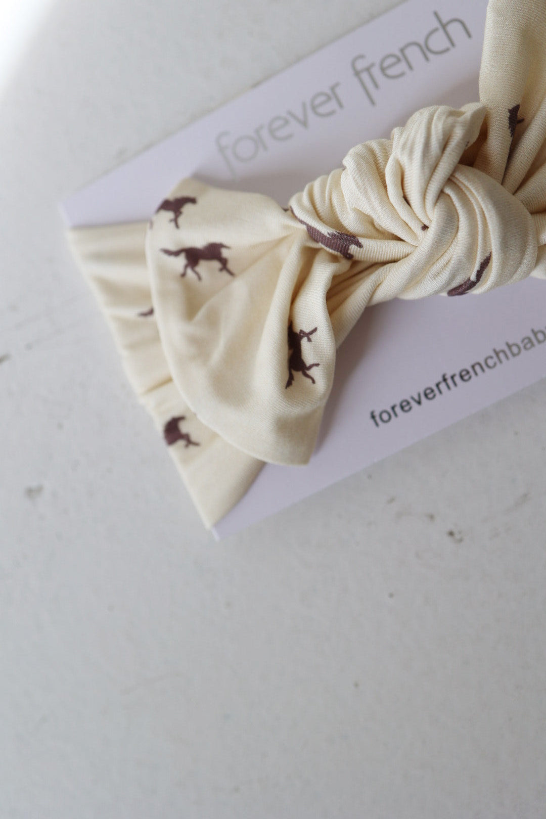 The Bamboo Head Wrap | Wild Horses by forever french baby features cream fabric with small brown horse silhouettes, shown on a branded card against a light surface.