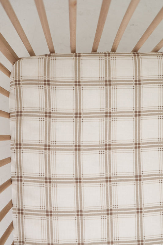 A top view of a crib with light wooden slats and a mattress covered in the forever french baby Muslin Crib Sheet | Ellis Plaid, perfect for adding cozy style to your baby nursery bedding.