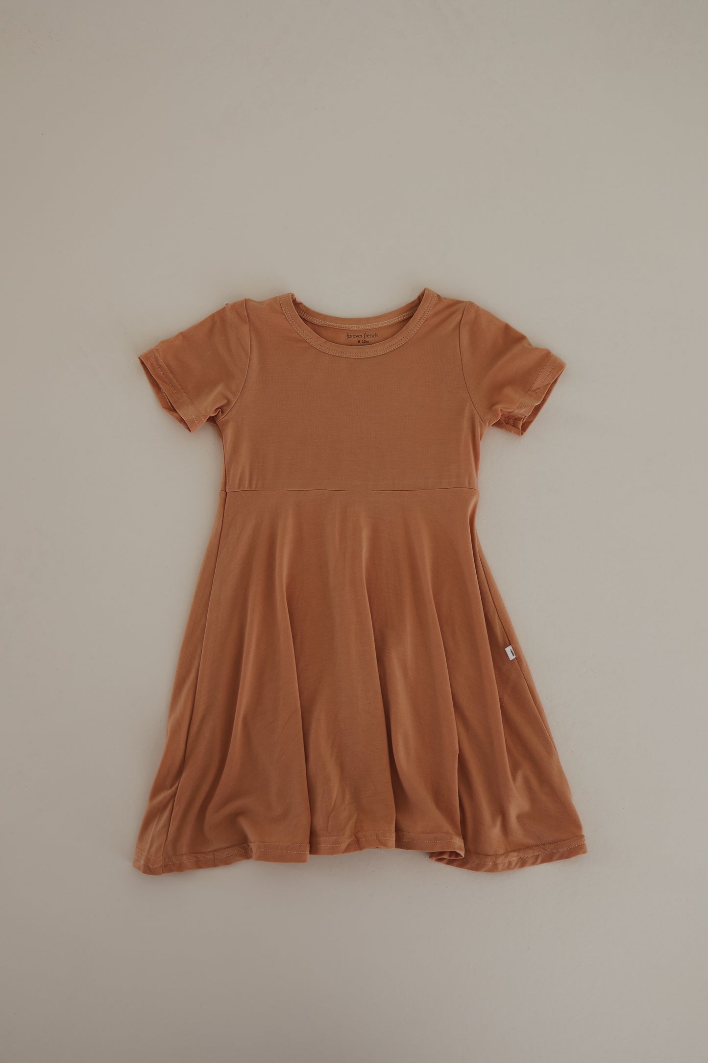 The Bamboo Dress | Clay by forever french baby is a small, short-sleeve, orange-brown dress with a round neckline, crafted from breathable fabric. It boasts a fitted bodice and a flared skirt, offering a simple and casual style.