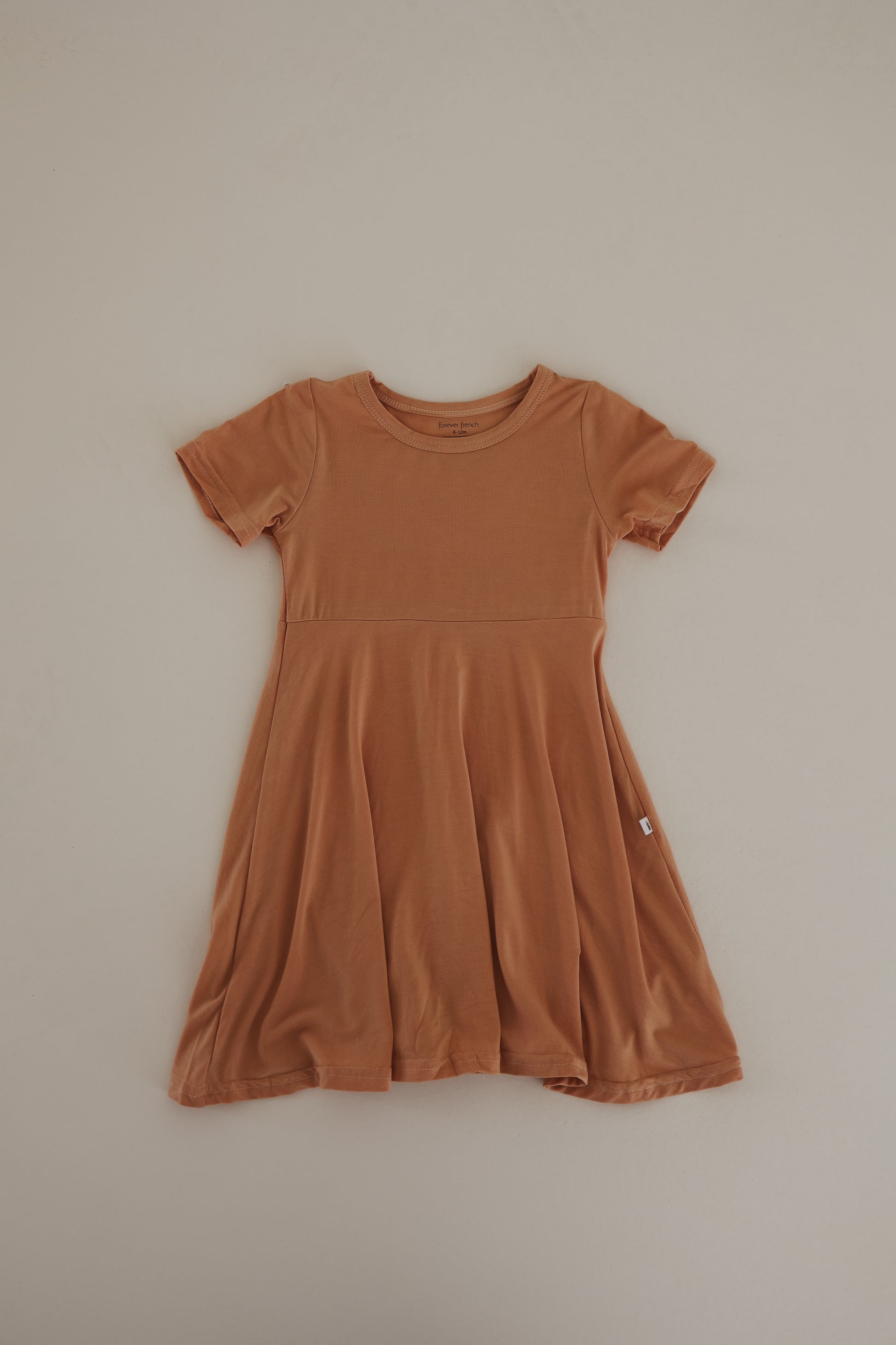 The Bamboo Dress | Clay by forever french baby is a small, short-sleeve, orange-brown dress with a round neckline, crafted from breathable fabric. It boasts a fitted bodice and a flared skirt, offering a simple and casual style.