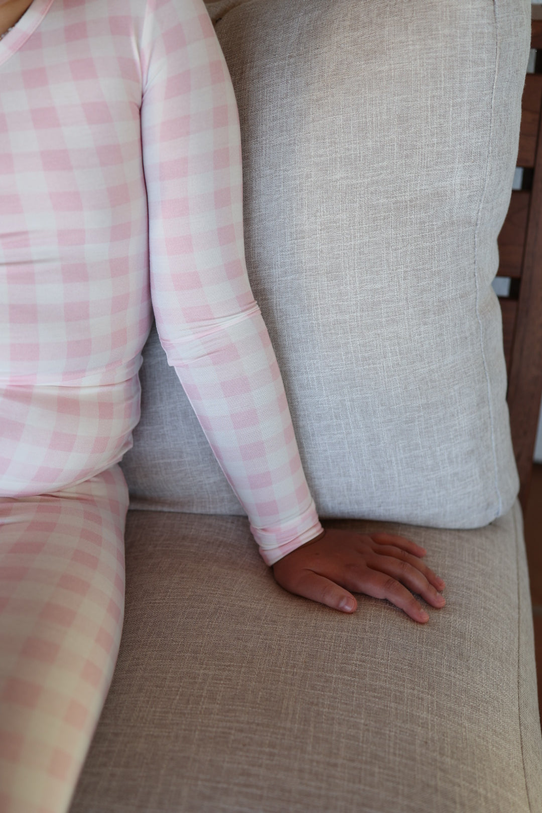 A child in forever french baby’s Bamboo Two Piece Pajamas | Pink Sugar sits on a light beige couch, with one arm and hand resting on the seat cushion.