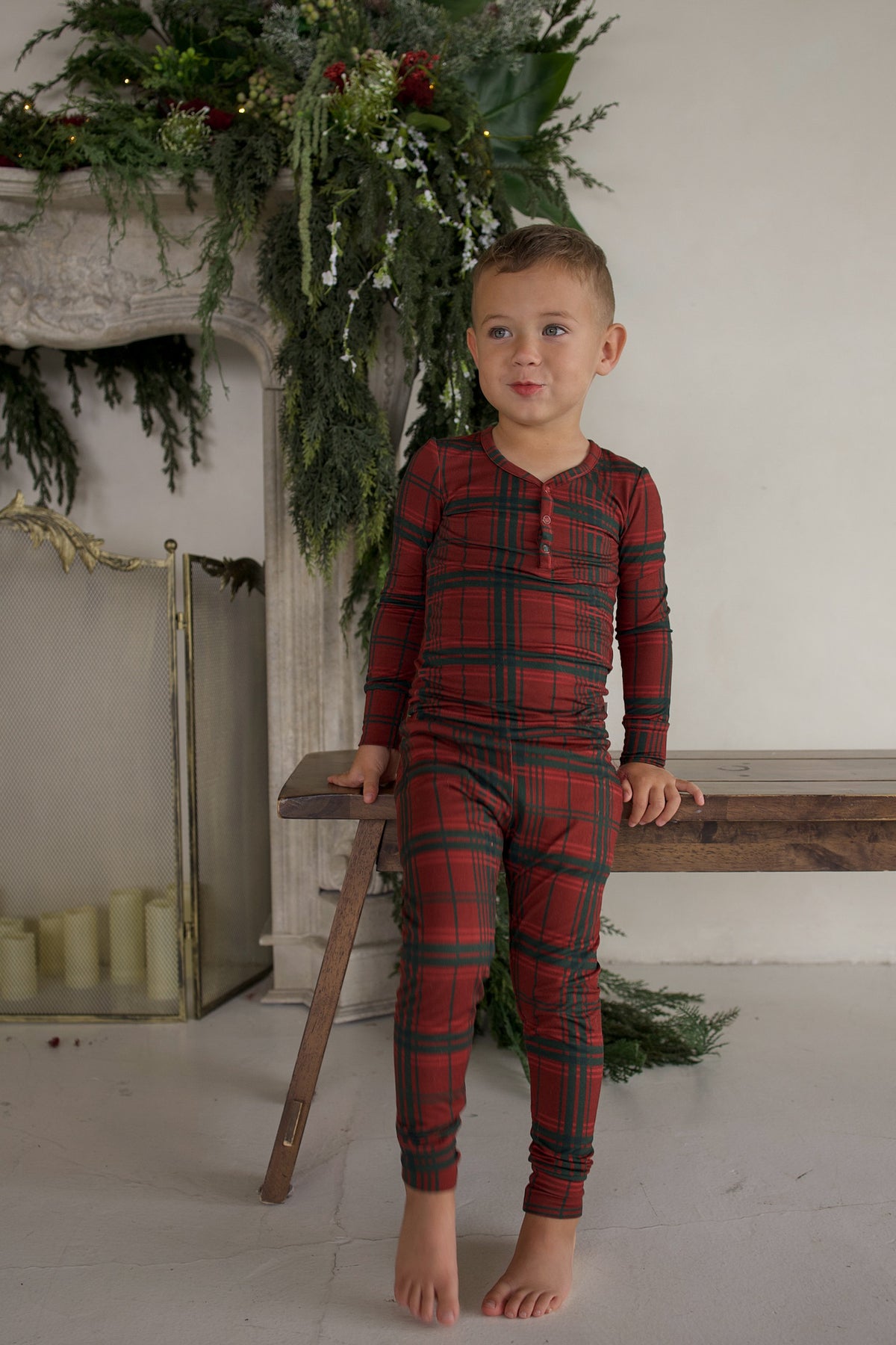 A young boy sits on a wooden bench wearing a long-sleeved Bamboo Two Piece Pajamas | Christmas Plaid set.