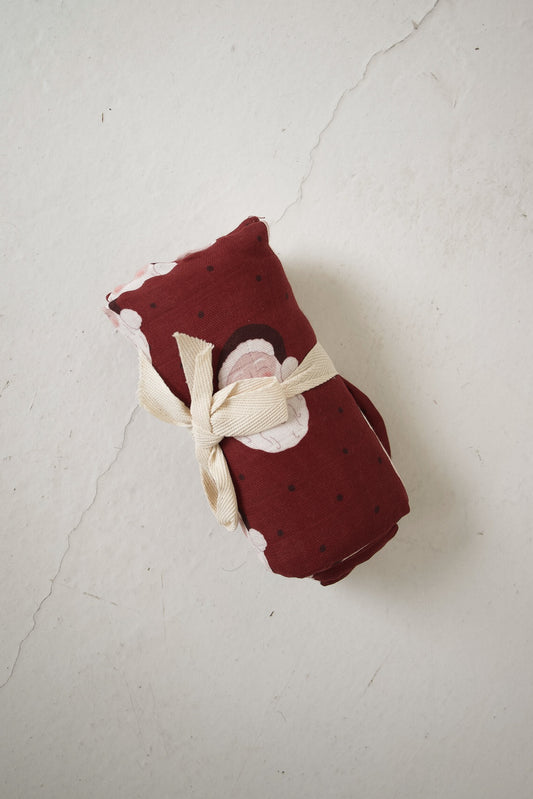 A dark red forever french baby Muslin Swaddle | Vintage Santa featuring a vintage Santa and polka dot pattern, rolled and tied with a cream ribbon.