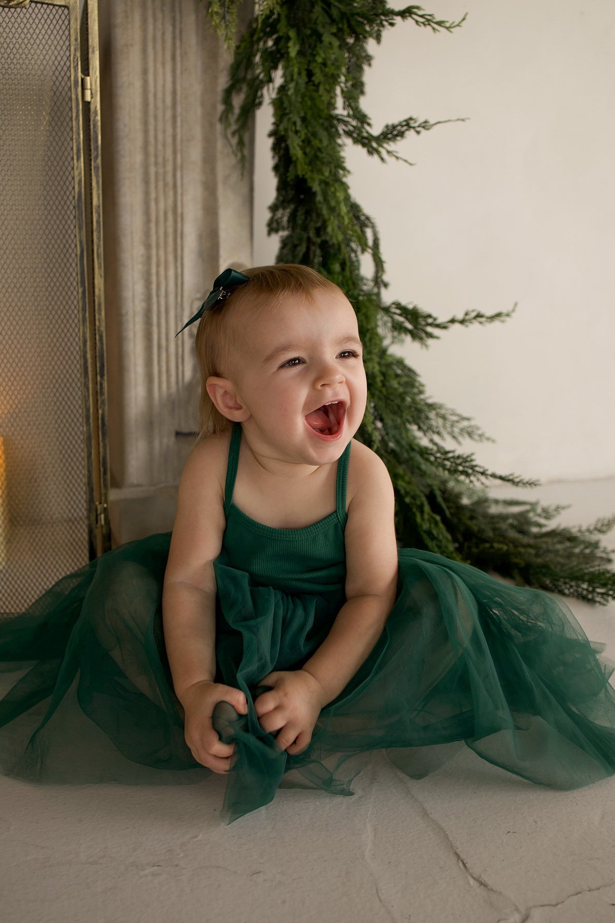 A toddler laughing while wearing a dark green ff Tutu Dress | Mistletoe featuring a layered tulle skirt and a matching hair bow.