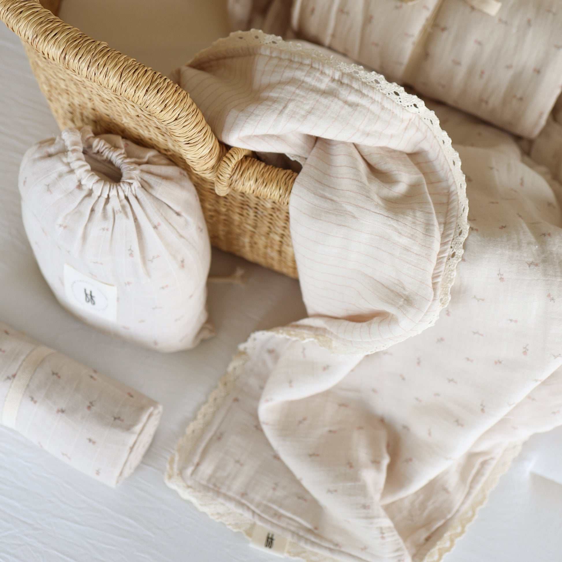 The Muslin Crib Sheet | Lucy by forever french baby, in soft cream cotton with delicate lace trim, rests on a white surface. Nearby are a matching pouch and blanket—perfect cozy touches for your floral nursery bedding.