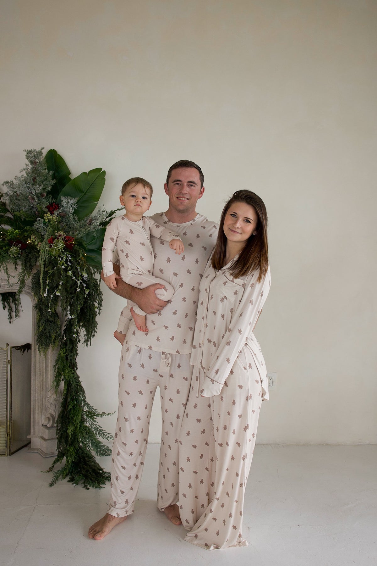 A man, woman, and toddler wear matching cream-colored bamboo Men’s Short Sleeve Pajamas | Gingersnap with a small gingerbread man print.