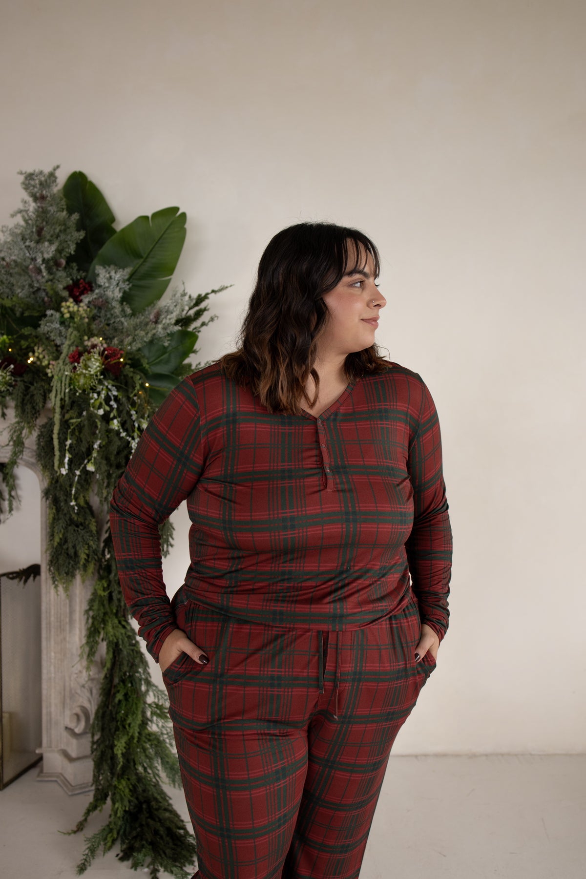 A woman wearing a Women’s Long Sleeve Bamboo Pajama | Christmas Plaid set featuring a red and green plaid top with a button placket and matching bamboo bottoms.