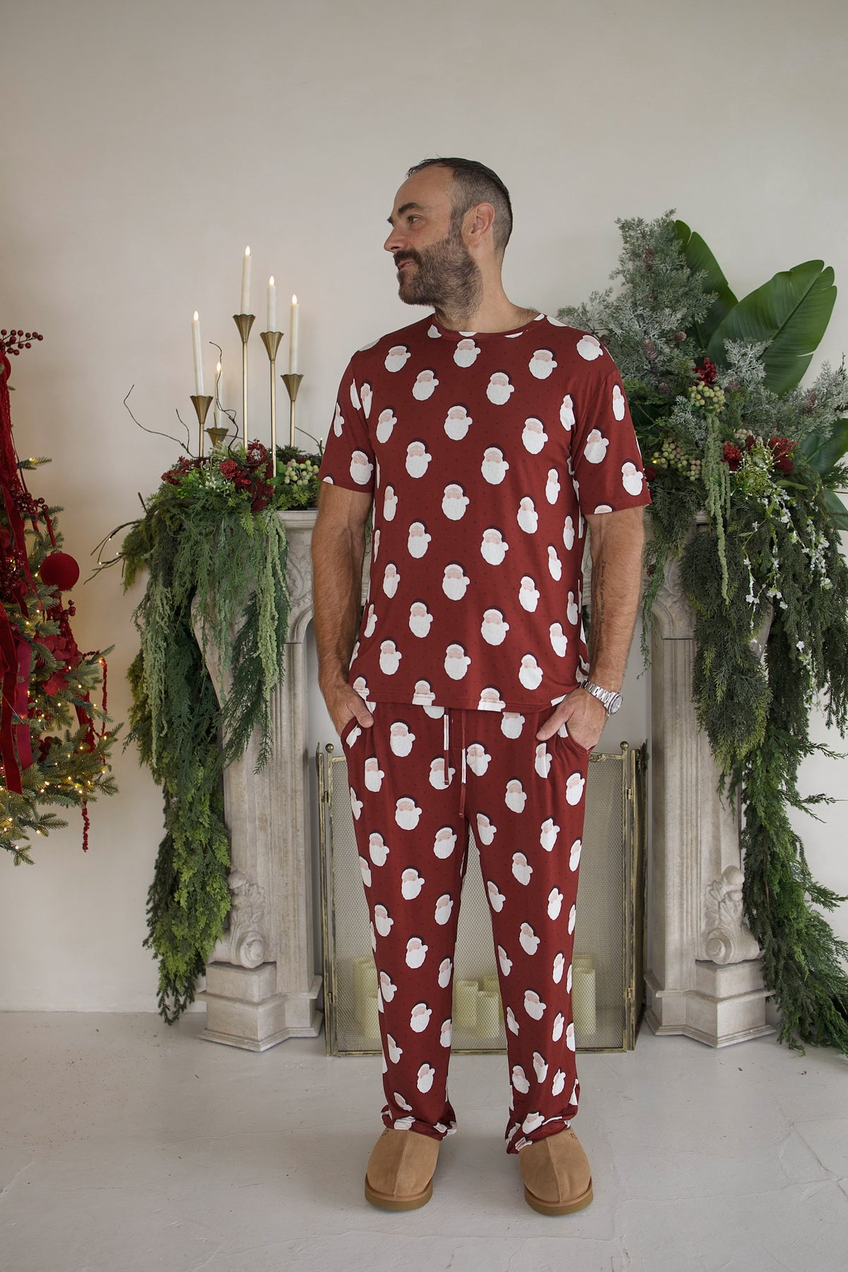 A man wears a Men’s Short Sleeve Pajamas | Vintage Santa set featuring a repeating pattern of white Santa Claus faces on a red background.