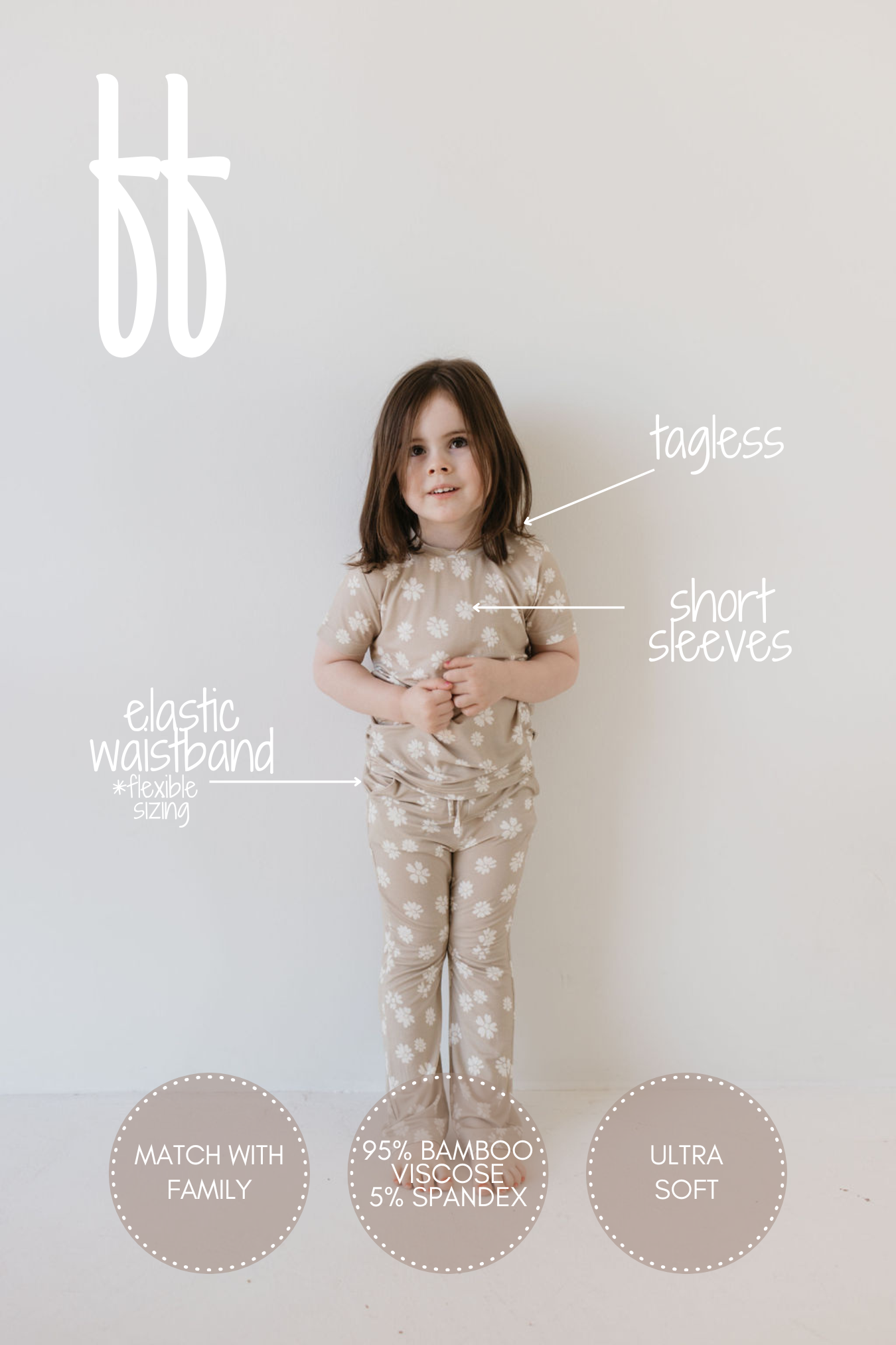 A young child is standing against a white wall wearing the Toddler Short Sleeve Bamboo Lounge Set in beige with white patterns. Created by forever french baby, these tagless pajamas feature short sleeves and an elastic waistband, made from 95% bamboo viscose and 5% spandex. They are celebrated for their ultra-soft, hypoallergenic, and breathable qualities, making them ideal for coordinating with family outfits.