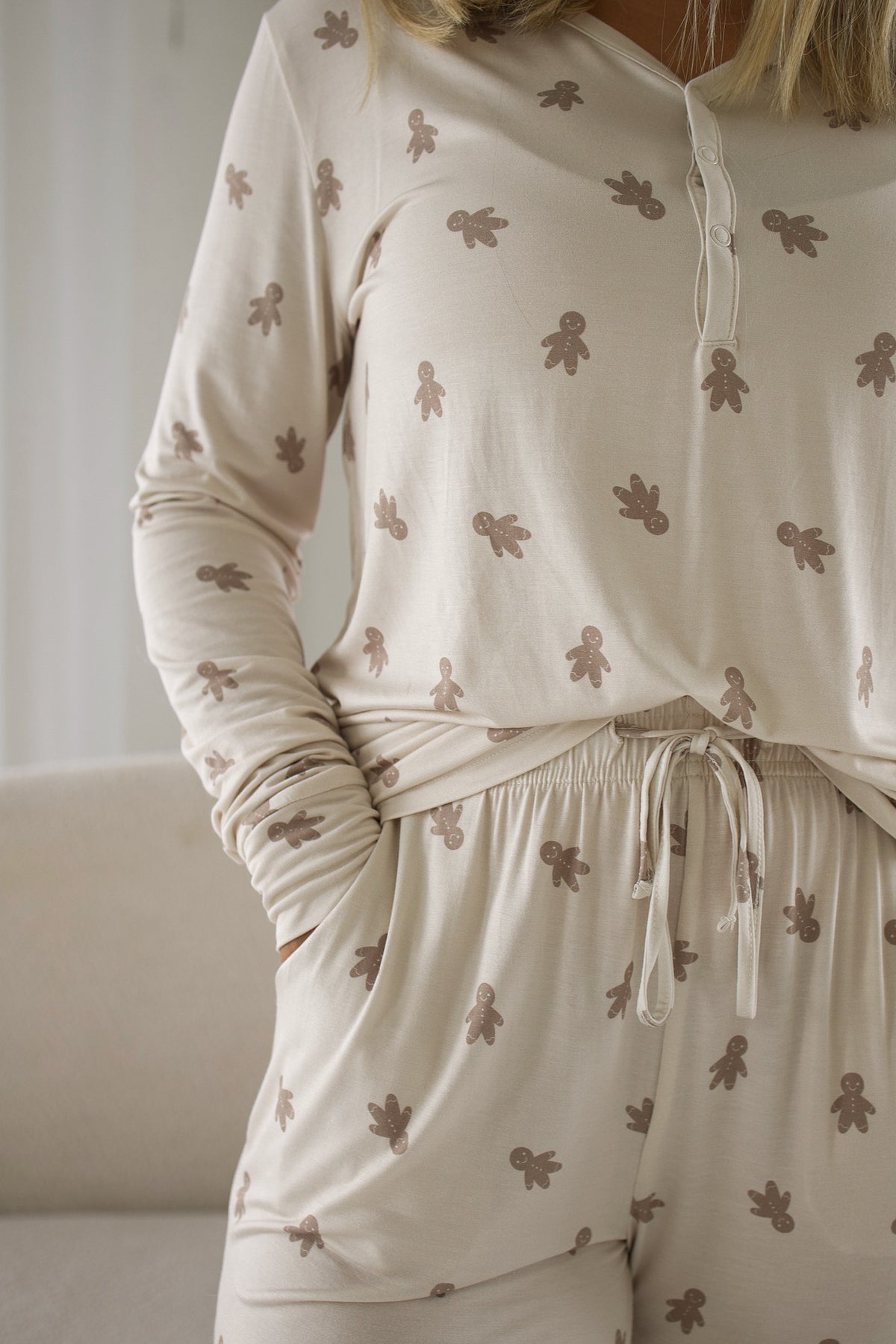 A person wearing a Women’s Long Sleeve Bamboo Pajama | Gingersnap set, featuring a long-sleeve henley top and matching pants with a brown gingerbread man print.