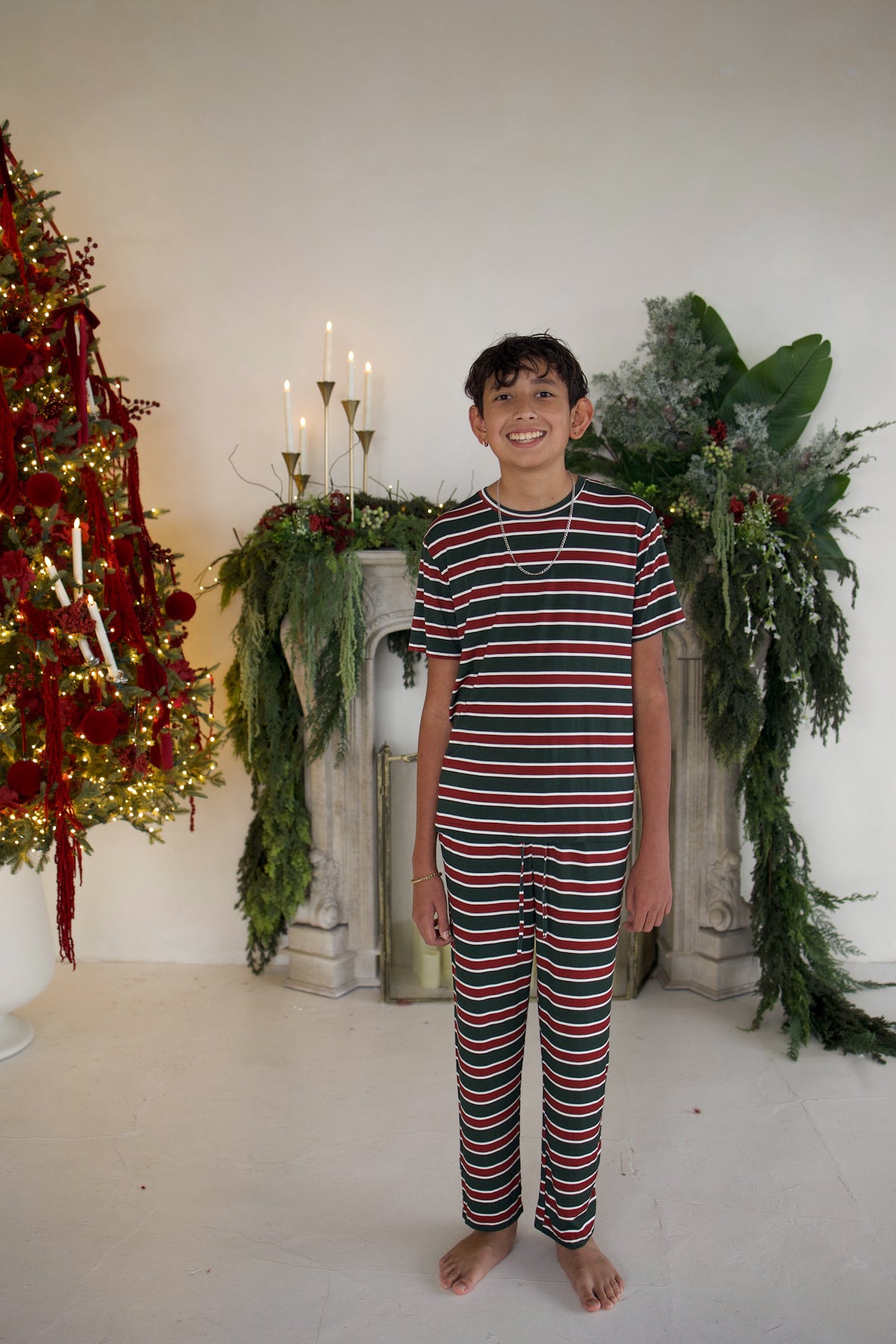 A pre-teen boy wearing Youth Straight Leg Bamboo Pajamas | Holiday Stripe, consisting of a short-sleeved shirt and matching straight-leg pants with a red, green, and white horizontal stripe pattern.