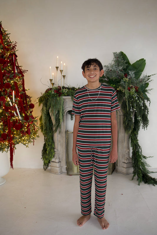 A pre-teen boy wearing Youth Straight Leg Bamboo Pajamas | Holiday Stripe, consisting of a short-sleeved shirt and matching straight-leg pants with a red, green, and white horizontal stripe pattern.