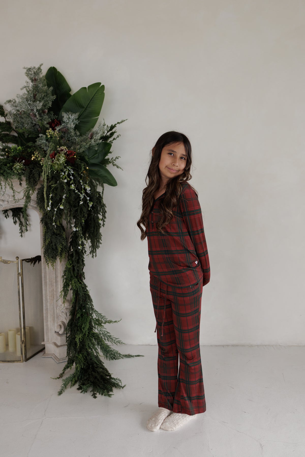 A young girl smiles wearing red and green plaid Youth Flare Bamboo Pajamas | Christmas Plaid, featuring long sleeves and flared bottoms.