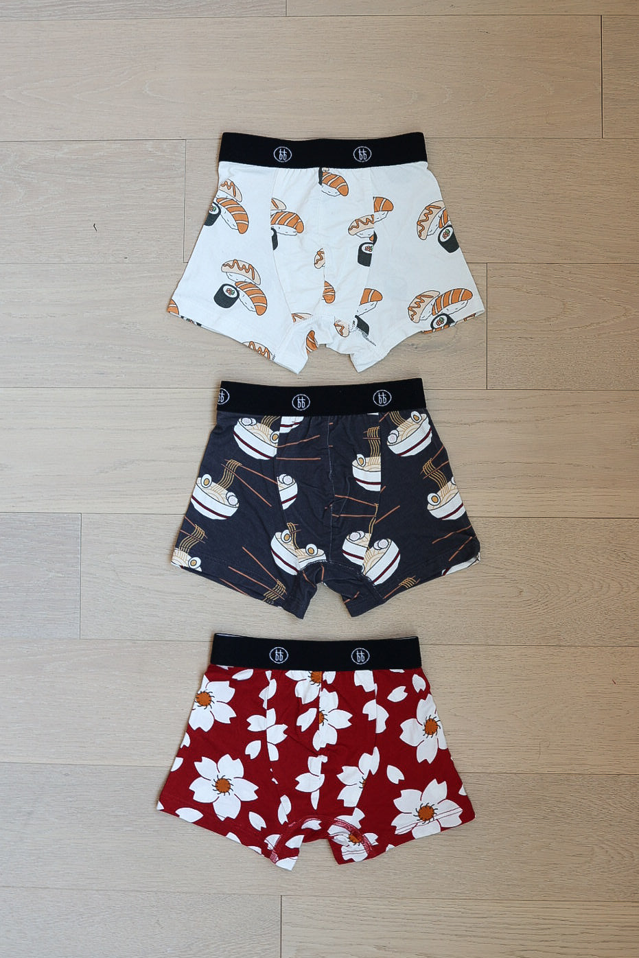 Three pairs of forever french baby Bamboo Boxers (Cherry Blossoms, Ramen & Sushi) are laid flat: one with sushi print, one with ramen bowls, and one with a white and yellow cherry blossom pattern.