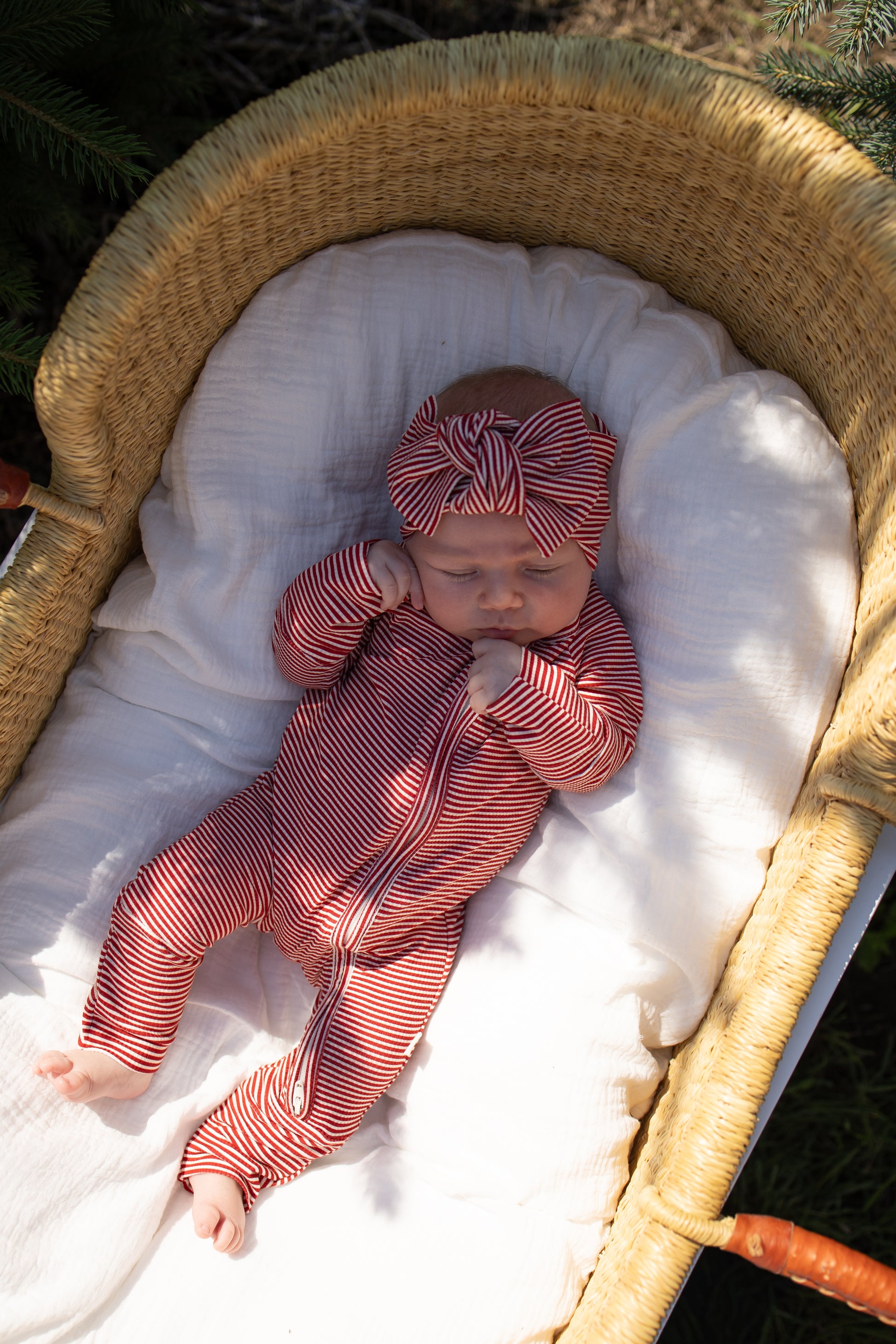 A baby sleeps peacefully in a wicker bassinet lined with a white blanket, outdoors in natural light, wearing the forever french baby Bamboo Head Wrap | Peppermint Stripe Ribbed.
