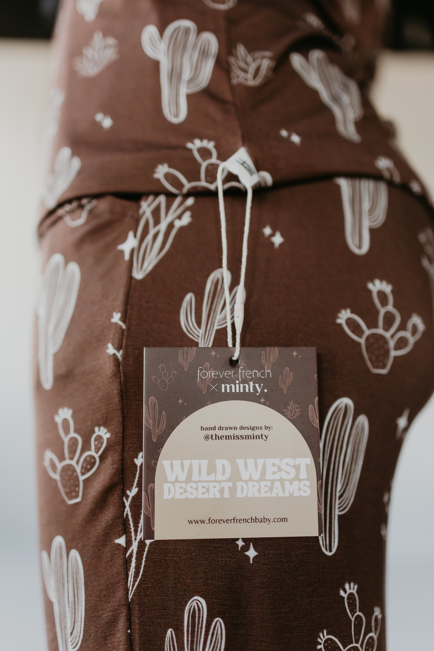 A close-up of the brown bamboo pajamas featuring white cactus illustrations shows a tag reading "Minty x FF Wild West Desert Dreams." This collaboration between Forever French Baby and Minty highlights hand-drawn designs on hypoallergenic fabric.