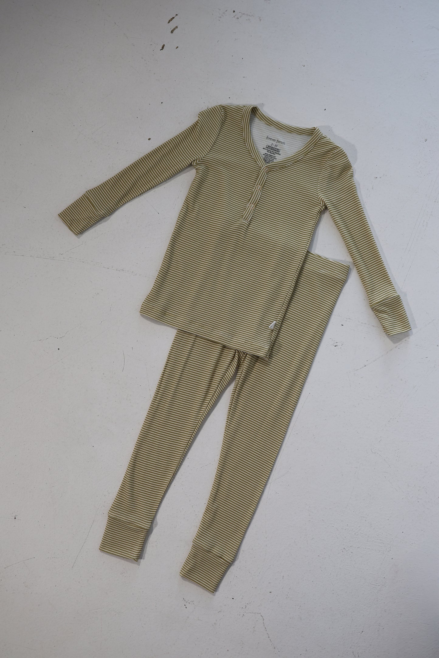 The Bamboo Two Piece Pajamas | Willow Stripe Ribbed by forever french baby, a light beige, long-sleeve set with thin dark stripes and henley top, is hypoallergenic kids clothing laid flat on a white surface.