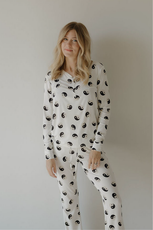A woman with long blonde hair wears the forever French baby Women's Bamboo Pajama in Black & White Yin Yang, featuring a breastfeeding-friendly design and elastic waistband, while smiling softly at the camera against a light background.
