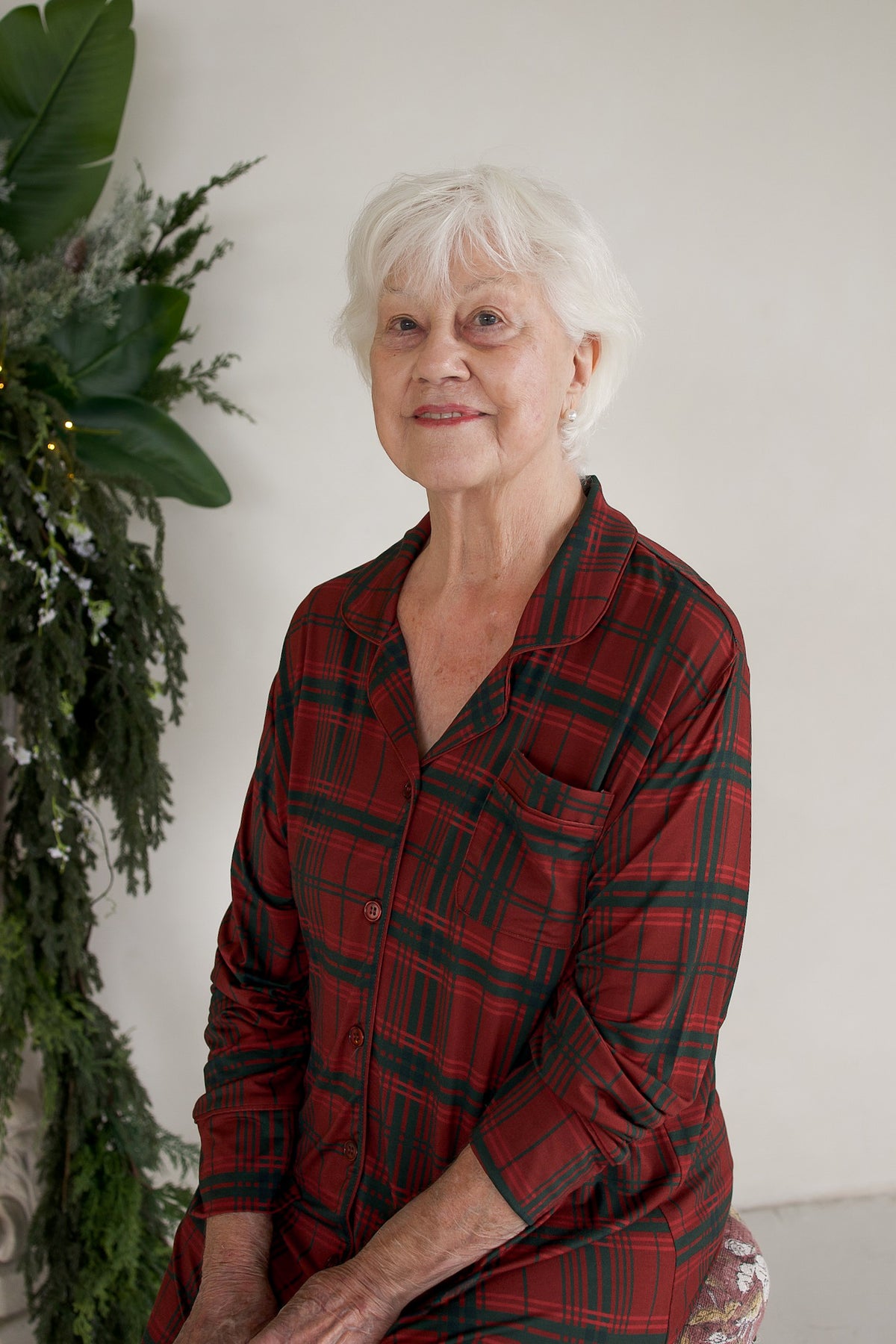An elderly woman with short white hair wearing a long-sleeved Women’s Bamboo Sleeping Dress in Christmas Plaid.