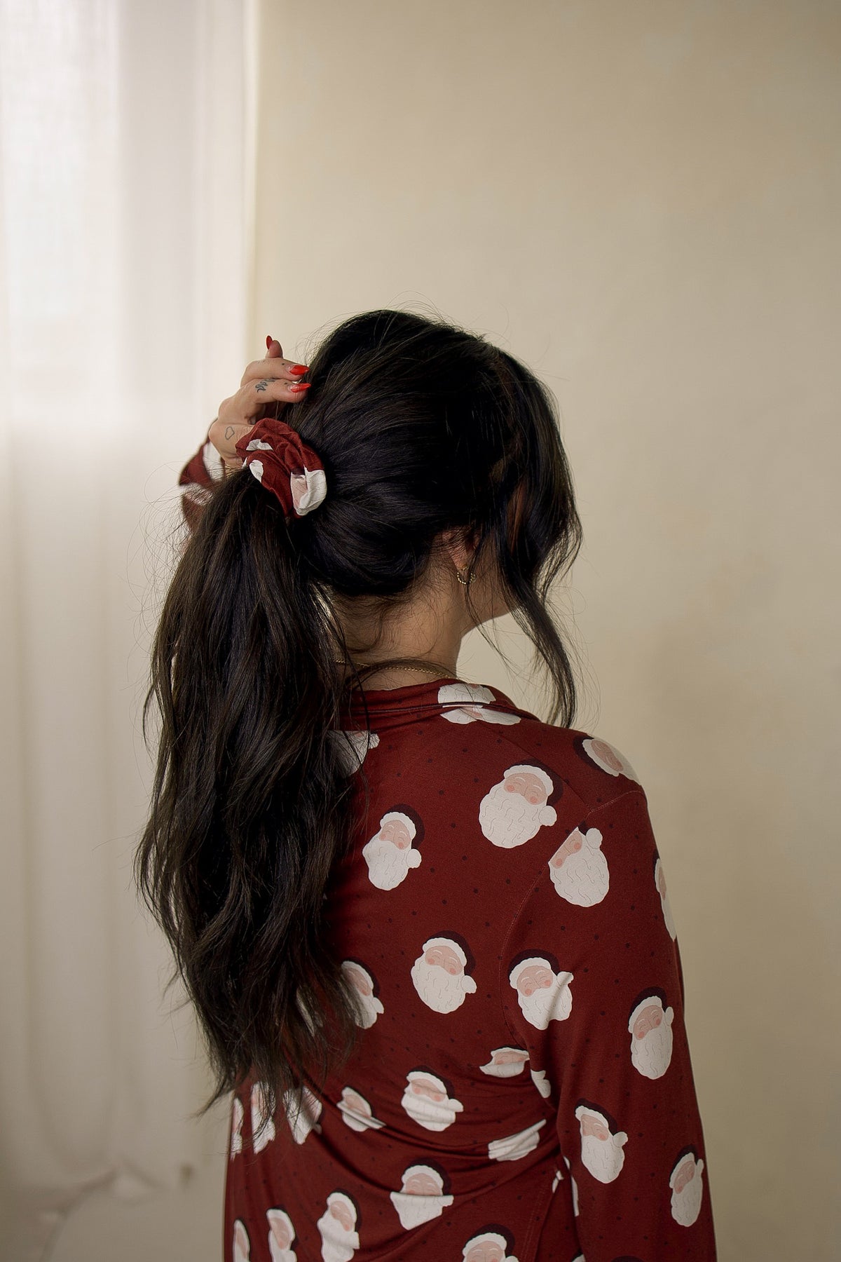 A person wearing a ponytail secured with a forever french baby Scrunchie | Vintage Santa, matching a long-sleeved shirt with the same vintage Santa print.