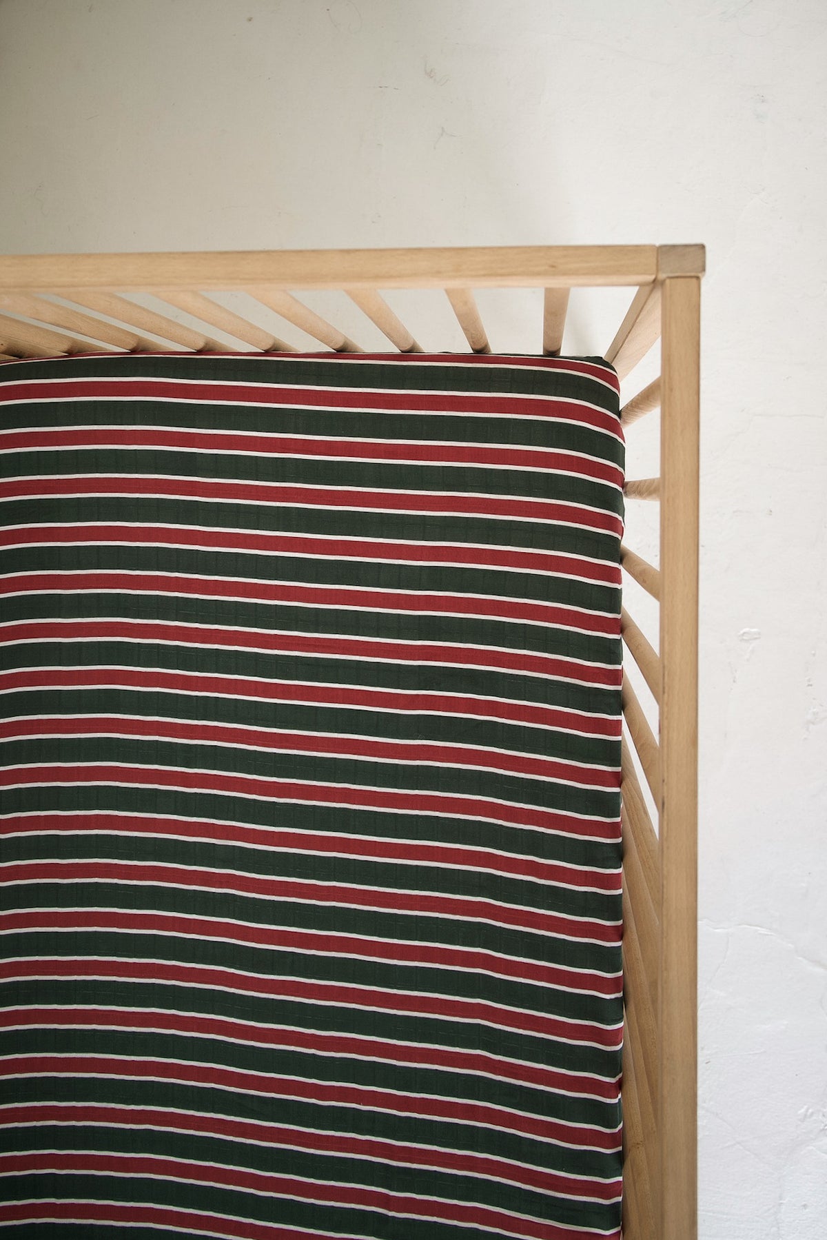 Forever French Baby Muslin Crib Sheet | Holiday Stripe featuring a pattern of horizontal red, dark green, and white stripes covering a crib mattress.