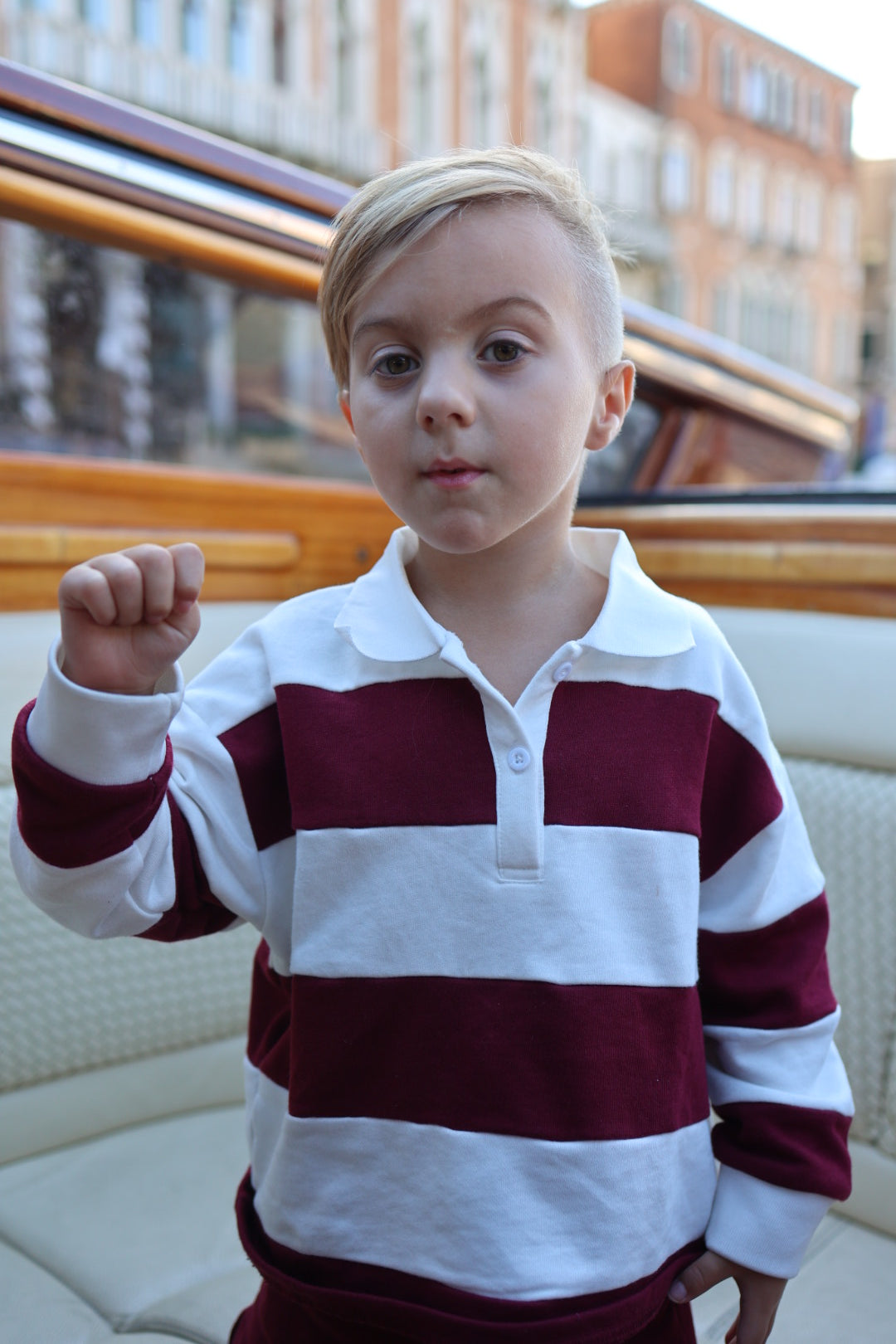 A young child wearing a long-sleeved Child Rugby Sweatshirt | Deep Cranberry featuring horizontal white and dark red stripes.
