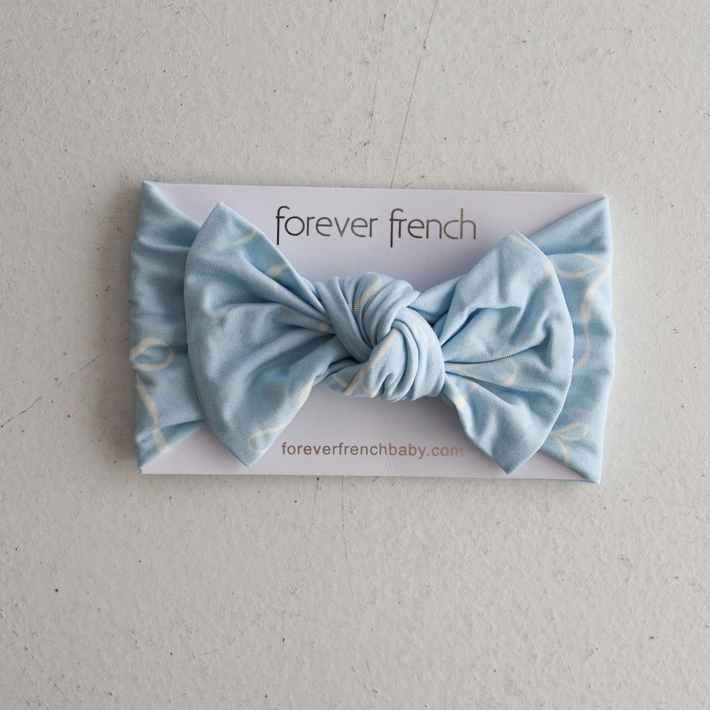 A Bamboo Head Wrap | Blue Bows by forever french baby is shown with a large light blue bow on its card, set against a light textured background.