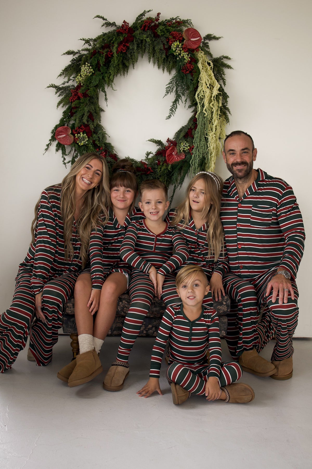 A family of six wearing Men’s Bamboo Button Up Lounge Set | Holiday Stripe in red, green, and white stripes, posing in front of a large holiday wreath.