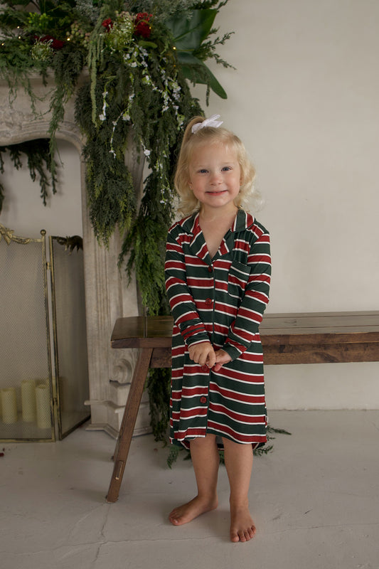 A young girl wearing a Bamboo Sleeping Dress | Holiday Stripe, a long-sleeved nightshirt with red, white, and green horizontal stripes.