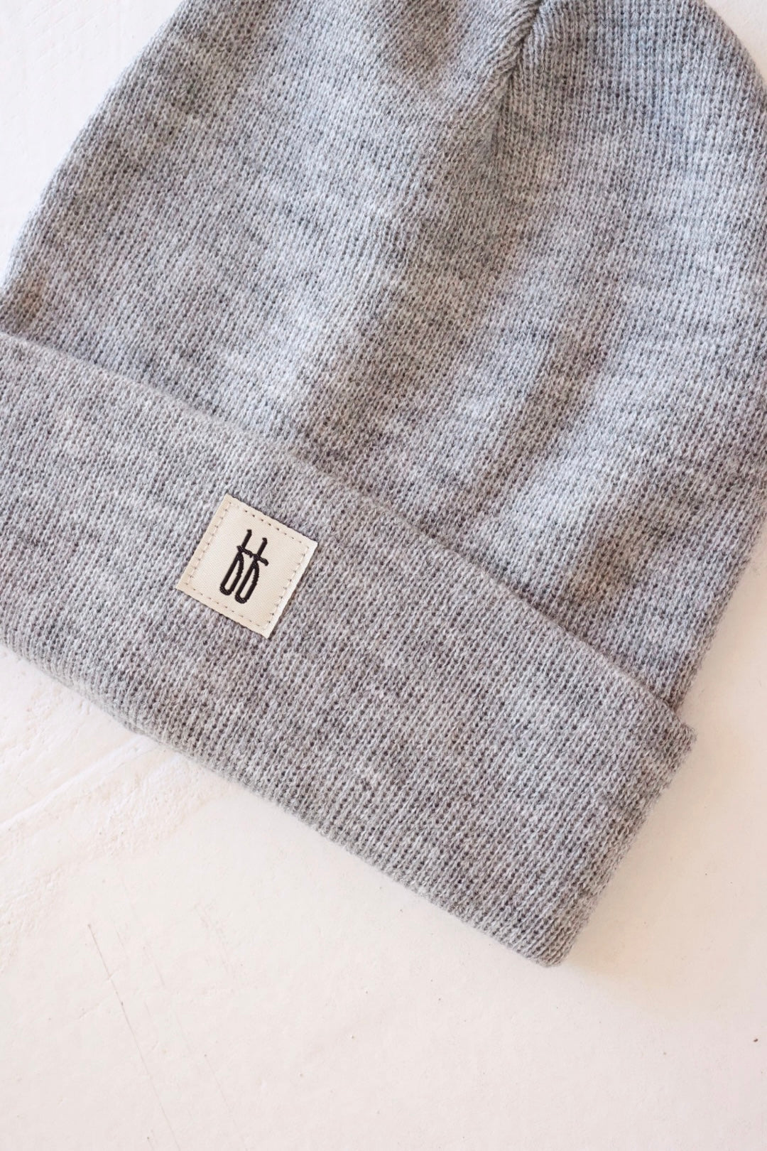 The forever french baby ff Knit Beanie | Adult is displayed on a white surface. With its ribbed design, this gray beanie features a folded brim adorned with a small, rectangular white label showcasing the brand's black stylized logo. The texture of the breathable yarn is visible, giving the beanie a cozy appearance.