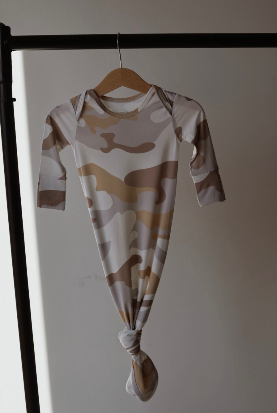 The forever french baby Bamboo Knotted Gown | Camo 2.0, featuring a brown, beige, and white camouflage print, hangs tied at the bottom on a wooden hanger against a neutral background—a hypoallergenic essential for newborns.