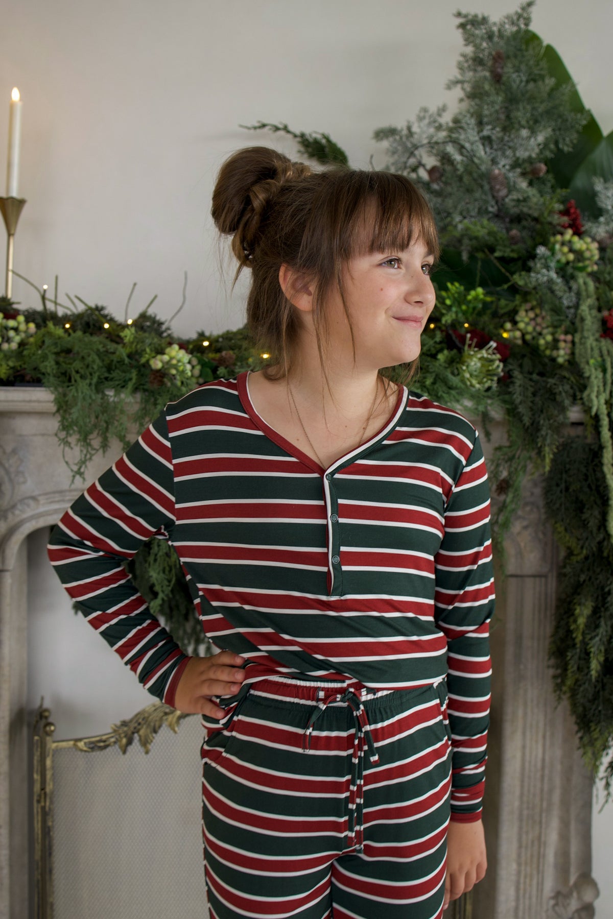 A young person wearing Youth Flare Bamboo Pajamas | Holiday Stripe, featuring a long-sleeved top and pants in a red, green, and white horizontal stripe pattern.