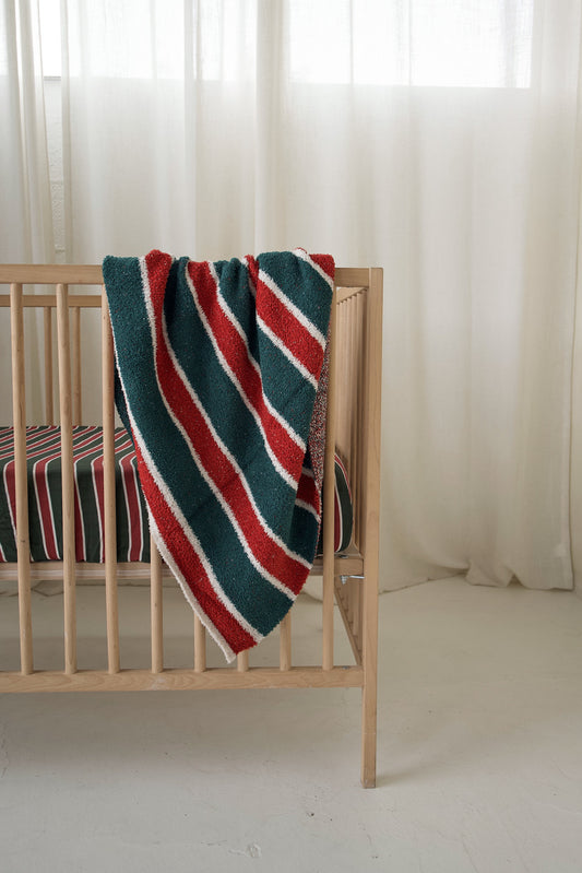 *PRE-ORDER* Plush Blanket | Holiday Stripe by forever french baby in an Oeko-Tex certified microfiber with a green, red, and white holiday stripe pattern draped over a wooden crib.