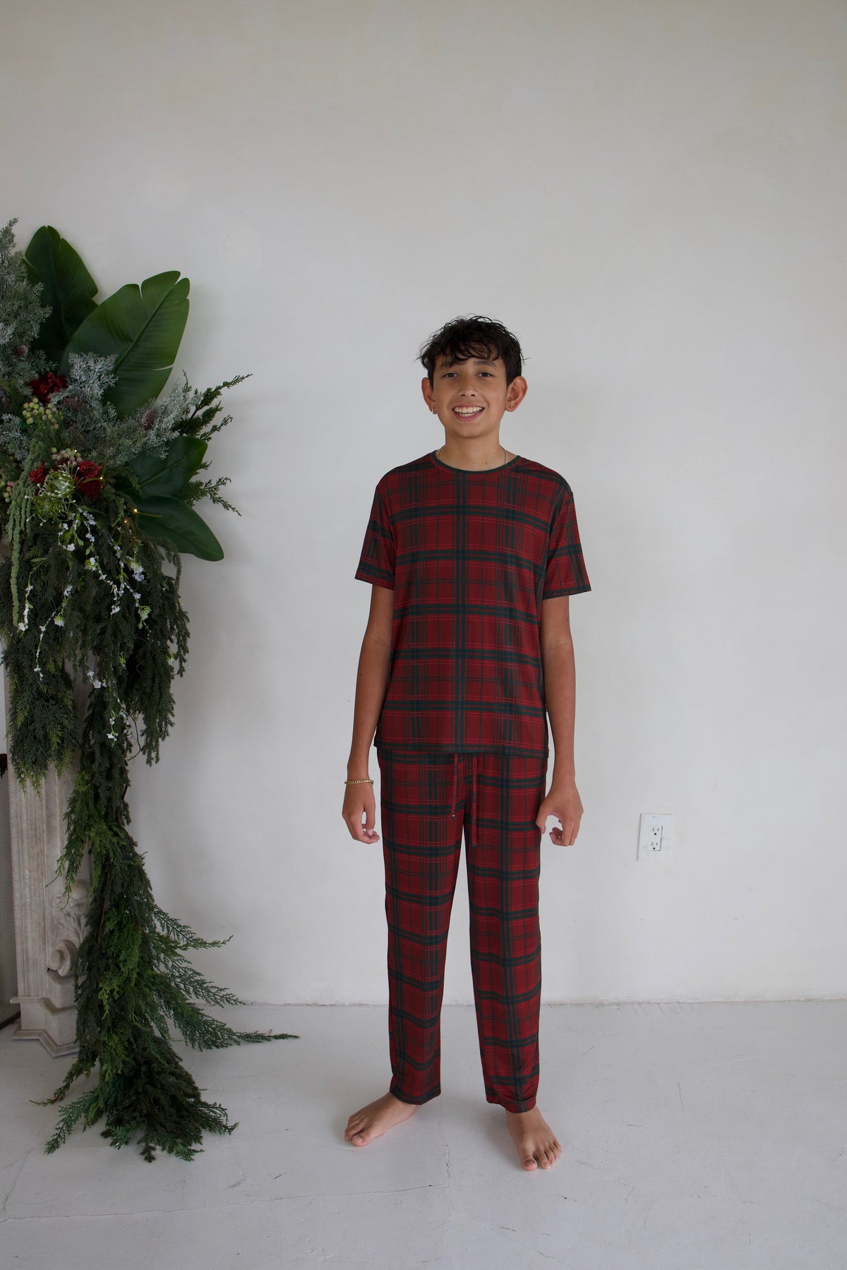A pre-teen boy wearing Youth Straight Leg Bamboo Pajamas in Christmas Plaid, consisting of a short-sleeved red and green plaid top and matching pants.
