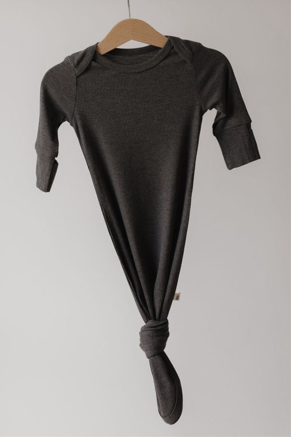 The forever french baby Bamboo Knotted Gown in Shadow, a dark gray hypo-allergenic long-sleeve baby gown with a knotted bottom, hangs on a wooden hanger against a plain neutral background.
